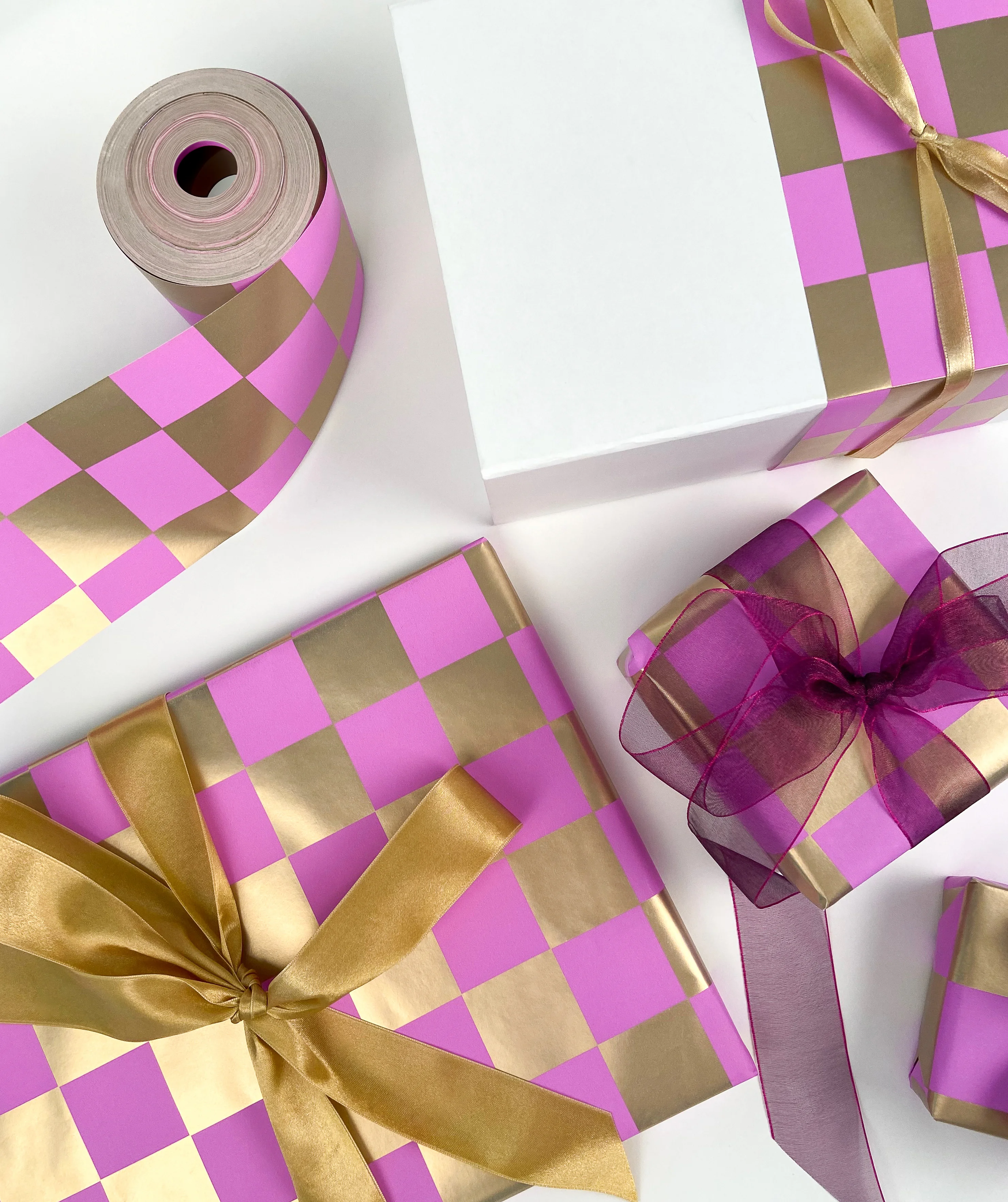 golden checkers pink gift wrap styled with a white magnetic closure gift box and true gold satin ribbon. pictured on a white background.